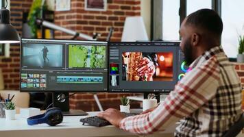 African american freelancer editing a background at his home office, mixing clips on dual monitors. Professional man employs tech tools for creative and multimedia projects. Camera B. video