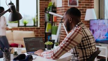 africano americano Programas desenvolvedor trabalho em programação código em uma computador portátil dentro controlo remoto área de trabalho. produtivo isto engenheiro trabalhando em codificação, Programas Projeto e Internet segurança inovação. Câmera b. video