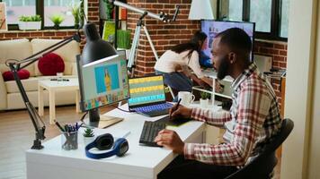 African american male designer edits images on dual monitors, computer setup in a creative office. Ideal workspace for digital media professional focused on photo retouching. Camera A. video