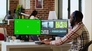 Male editor works on a movie project in a creative software next to chroma key, multitasking between timeline editing and color grading using dual monitors and tech tools. Camera B. video
