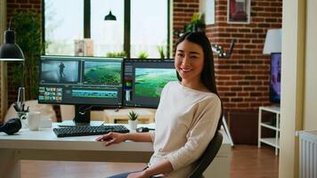 Asian woman editor working with dual monitors in living room, editing footage and color grading in a modern office setup. Perfect for post production and media creation. Camera A. video