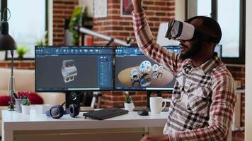 Male 3D engineer developing an industrial prototype with vr headset, using artificial intelligence and professional CAD software on dual monitors. African american freelancer at home. Camera B. video