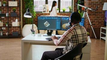African american industrial designer works on CAD software and listens to music, multitasking at home. Engineer specialist uses digital tools and 3D modeling for industrial projects. Camera A. video