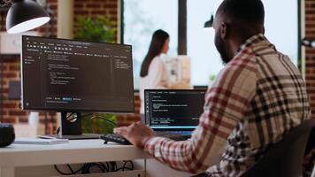 africano americano isto profissional tipos programação código em dual monitores dentro casa escritório, trabalhando em Programas desenvolvimento e Internet segurança. ideal configuração para controlo remoto trabalhos e produtividade. Câmera b. video