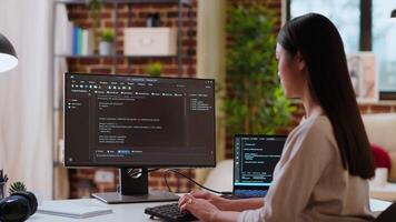 Asian woman is seen typing code for an app development project on her computer, working from a home office. IT specialist engineer focuses on software programming and remote tech work. Camera B. video