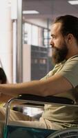 Vertical IT worker with disability sitting in wheelchair in office working at computer desk, focused on testing programs. Software engineer with paraplegia in inclusive workplace checking code on PC, camera A video
