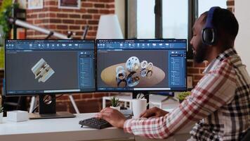 African american industrial designer works on CAD software and listens to music, multitasking at home. Engineer specialist uses digital tools and 3D modeling for industrial projects. Camera B. video