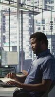 Vertical System administrator in office yawning during shift, feeling tired while looking at software interface on PC. Exhausted man being sleepy in workspace, programming on computer monitor, camera B video