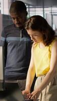 Vertical African american supervisor looking at laptop screen with employee, checking on finished project task. Company management executive and woman analyzing data on notebook, camera A video