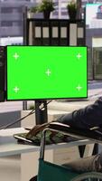 Vertical Person with disability testing and deploying programs and systems on green screen PC. Software technician in wheelchair checking code on mockup PC, sitting at desk in office, camera A video