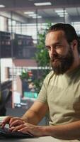 Vertical Employee looking at PC monitor, drinking coffee, checking data needed for finding business insights and finishing project task. Man analyzing data on computer, enjoying beverage, camera B video