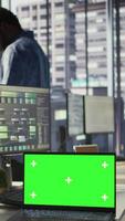 Vertical Green screen laptop on desk in workspace with admins in background doing software quality assurance. Chroma key notebook in office with woman at work inspecting coding on device, camera B video