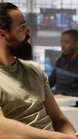 Vertical Worker sitting at office desk using computer during job shift, being interrupted by manager to receive info. Company employee in workspace doing tasks, listening to feedback from his boss, camera A video