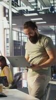 Vertical Admin at office desk utilizing cloud computing resources on laptop to train large scale machine learning models. Man monitoring company systems using notebook while standing in workspace, camera B video