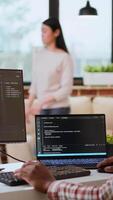 Vertical Male coder works from home typing code on a laptop in a modern living room. African american IT engineer using programming language and cloud computing for software development. Camera B. video