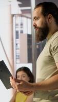 Vertical Cheerful admin holding laptop chatting with colleagues while working with machine learning tech. Man transforming data into predictive models using notebook and talking with coworkers, camera A video