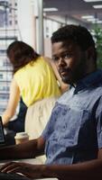 Vertical Man checking paperwork details on computer screen, solving tasks. African american bookkeeper in office making sure documents are compliant with quality assurance expectations and standards, camera B video