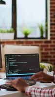 Vertical Young man seen programming software code on his laptop in a sleek home office. Workspace with dual monitors helps with software engineering, web development and coding productivity. Camera B. video