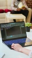 Vertical Asian female programmer works on coding software in a home office setup, typing code on a laptop. IT expert uses digital tools for multitasking, software development and app development. Camera A. video