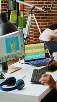 Vertical African american male designer edits images on dual monitors, computer setup in a creative office. Ideal workspace for digital media professional focused on photo retouching. Camera A. video