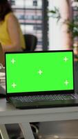 Vertical Green screen laptop on desk in workspace with admins in background doing software quality assurance. Chroma key notebook in office with woman at work inspecting coding on device, camera A video