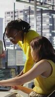 Vertical Admin assisted by coworker while utilizing cloud computing resources to train large scale machine learning models. Woman and colleague monitoring AI company systems using computer, camera B video