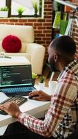 Vertical Young man seen programming software code on his laptop in a sleek home office. Workspace with dual monitors helps with software engineering, web development and coding productivity. Camera A. video