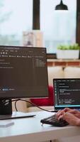 Vertical IT specialist types code on dual monitors in a cozy home office while working remotely. Asian woman uses programming language for productivity in coding and internet security. Camera B. video