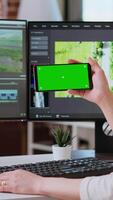 Vertical Female editor working on a creative project shoot, using chroma key copy space screen next to color grading software. Home workspace highlights productivity. Camera B. video