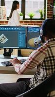 Vertical African american industrial designer works on CAD software and listens to music, multitasking at home. Engineer specialist uses digital tools and 3D modeling for industrial projects. Camera A. video