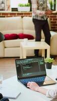 Vertical Software developer types programming code in a cozy home office setup. Asian woman coding for cloud computing on her laptop, enhances productivity for software development. Camera A. video