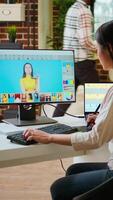 Vertical Asian graphic designer uses editing software for photo retouching in a well organized home workspace. Female freelancer uses digital tools essential for a creative artistic career. Camera A. video