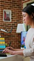 Vertical Asian creative woman edits photos using professional design software in a modern home office. Working with digital tools in the graphic design industry, retouching techniques. Camera A. video