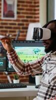 Vertical African american editor uses virtual reality glasses to do color grading, working with high tech vr headset and dual monitors at his home office. Filmmaker editing clips. Camera B. video