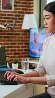 Vertical Professional software developer types code on a laptop in a sleek workspace. Asian female freelancer doing remote work on app development, software engineering and agile coding practices. Camera A. video