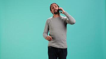 Joyous man catching up with friends in phone call using cellphone, studio background. Portrait of radiant person having conversation with mates during telephone call, camera A video