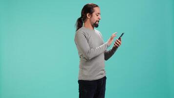 Joyous man with positive emotion enjoying talking with friends in phone call using smartphone, studio background. Happy person with smile on face, receiving good news during telephone call, camera A video