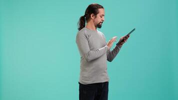 Portrait of upbeat person mindlessly scrolling on tablet screen, isolated over studio background. Cheerful man passing time on social media on portable device, enjoying leisure time, camera A video