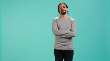Portrait of joyous man holding hands together, smiling, looking pleased, isolated over studio background. Upbeat person dressed casually exulting, feeling satisfied, camera A video