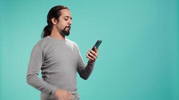 Joyous man with positive emotion enjoying talking with friends in phone call using smartphone, studio background. Happy person with smile on face, receiving good news during telephone call, camera B video