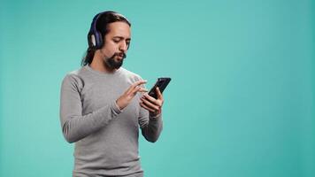 Relaxed man having fun listening to music from mobile phone, studio backdrop. Carefree person hearing tunes playing from smartphone device, isolated over studio background. camera B video