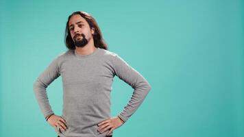 Portrait of man standing confidently with hands on hips, posing against plain studio background, projecting confidence and strength. Person holding assertive stance posture, camera B video