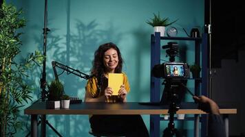 Excited content creator films review of book, browsing through pages, impressed by story. Online star giving her impressions of new novel release to readers, giving positive feedback, camera B video
