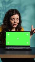 Vertical Influencer in home studio using recording tech to capture live broadcast, reviewing chroma key laptop. Online show host filming electronics haul, presenting green screen notebook for viewers, camera B video