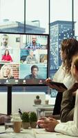Vertical Business team in a boardroom attend videocall meeting with investors group, discussing about increasing funds for a global development plan. Staff and shareholders on teleconference. Camera B. video
