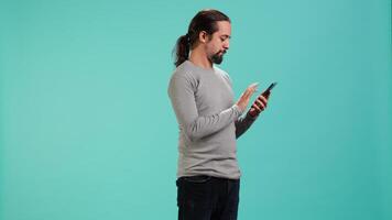 Portrait of smiling man scrolling on smartphone touchscreen, using mobile phone to check social media feed. Cheerful person browsing online websites, isolated over studio background, camera A video