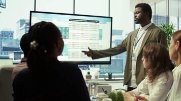 Business professional staff gather to review project development progress, detailed reports and statistics on interactive board to ensure strategic objectives. Diverse work team in meeting. Camera B. video