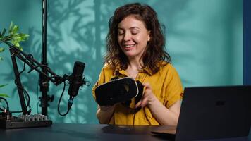 Happy tech content creator filming technology review of newly released VR glasses, unpacking them and presenting specs to fans. Jolly woman showing virtual reality headset to subscribers, camera A video