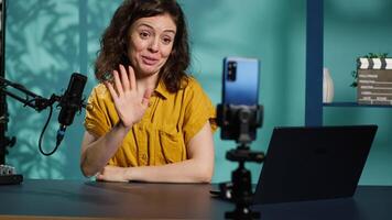 Influencer in home studio using smartphone on phone holder to record live broadcast, greeting subscribers. Internet star hosts q and a session with viewers using cellphone, camera A video
