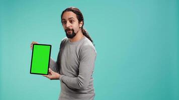 Jolly man presenting on green screen tablet, isolated over studio background. Upbeat person holding blank copy space chroma key device used for showcasing ads, camera B video